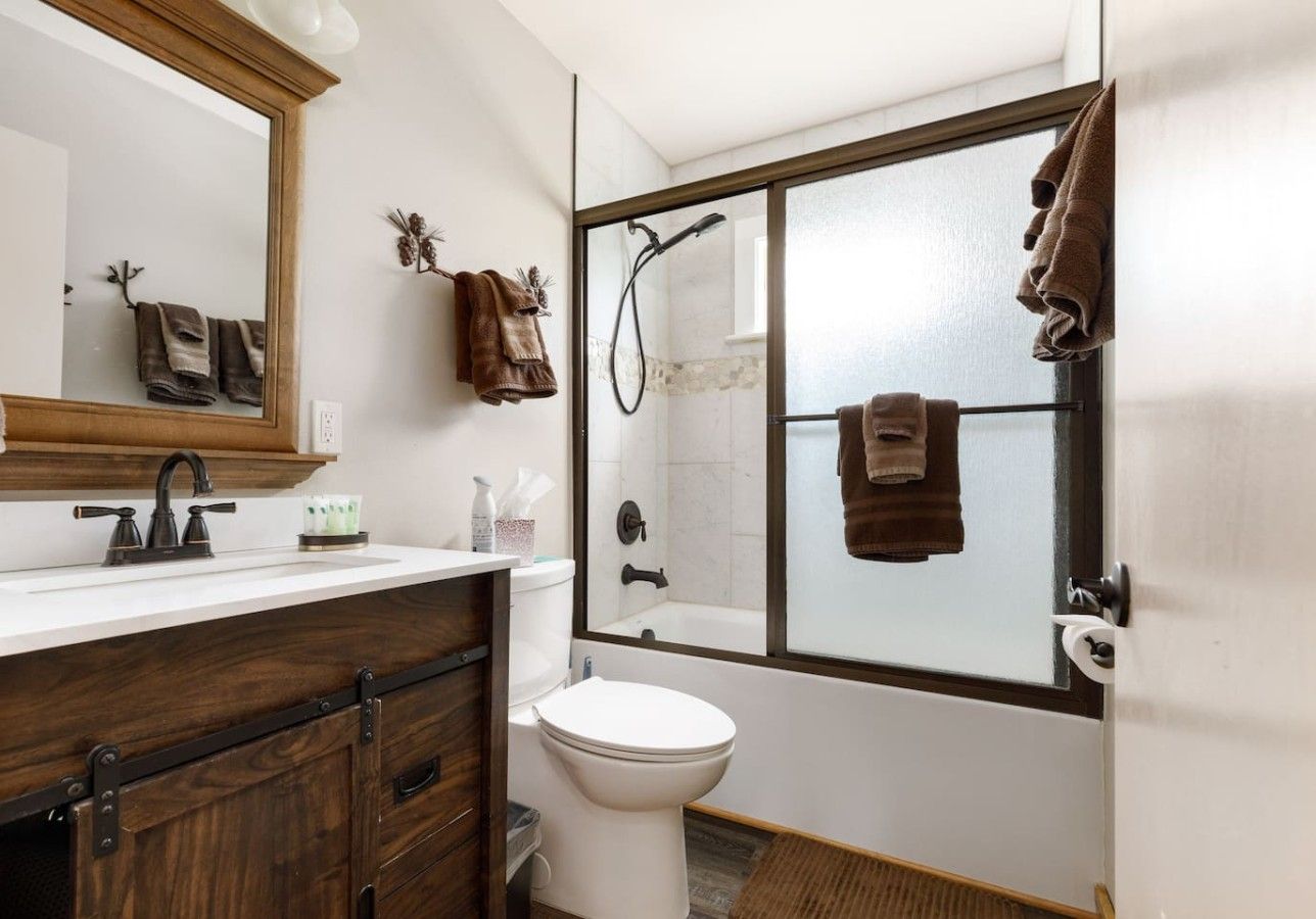 A bathroom with a wooden vanity, a white toilet, a shower with a glass door, and towels hanging on the wall.