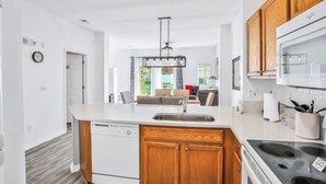 A modern kitchen with wooden cabinets, a built-in dishwasher, and a large island with a sink. - Central to all the fun Disney (Kissimmee)