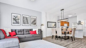 A modern living room with a grey sofa, red cushions, and a dining area with a table and chairs. - Central to all the fun Disney (Kissimmee)