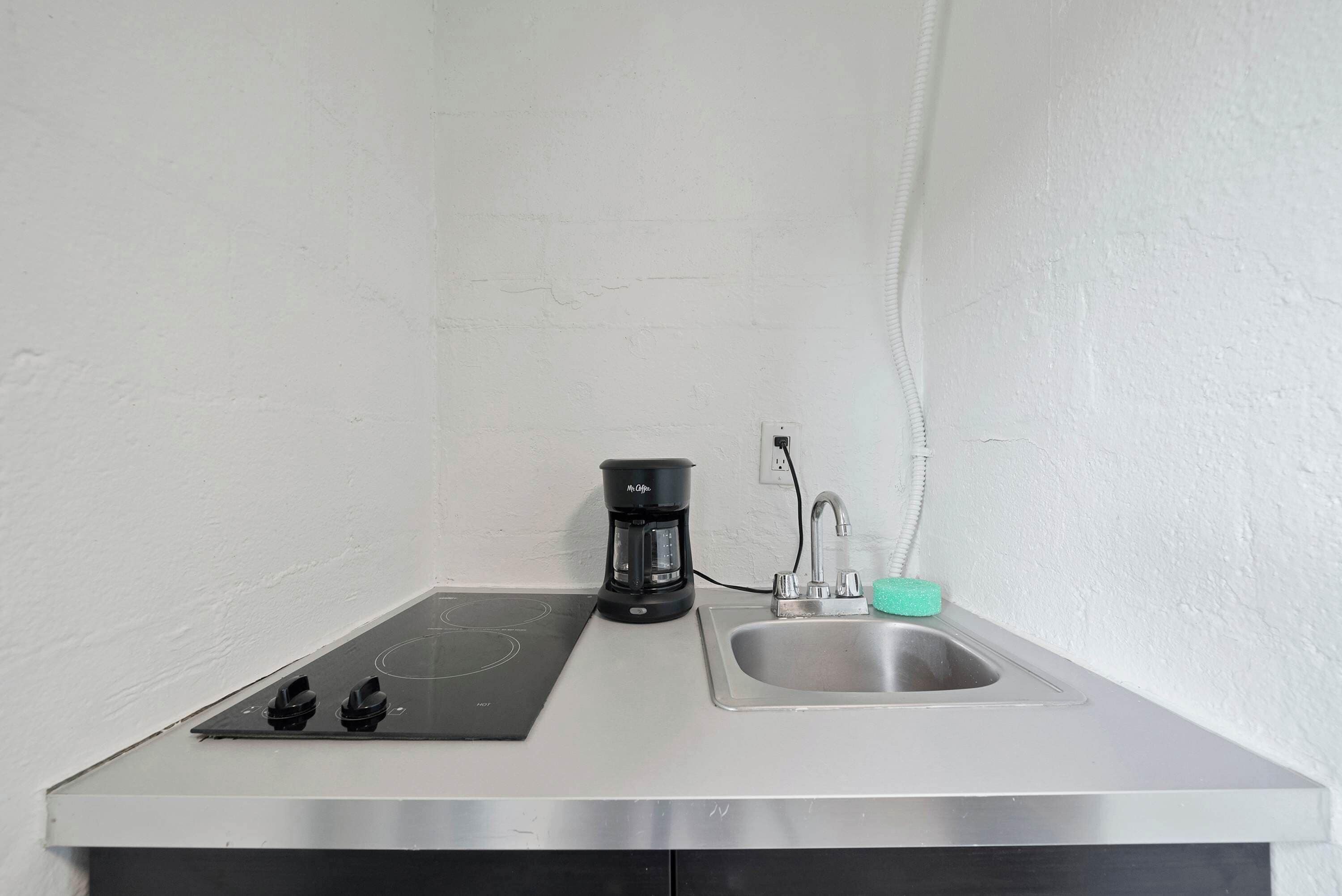 Una kitchenette equipada con una placa de inducción empotrada, una cafetera y un lavamanos de acero inoxidable.