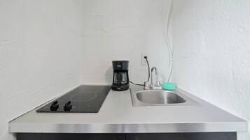 Una kitchenette equipada con una placa de inducción empotrada, una cafetera y un lavamanos de acero inoxidable.