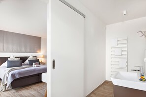 Ein modernes Schlafzimmer mit Bett, Nachttisch und einem Badezimmer mit Waschbecken und Spiegel.