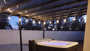 Un jacuzzi bajo un porche cubierto con guirnaldas de luces.