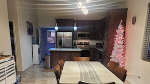 Comedor con una mesa lista para cuatro, un dispensador de agua y un refrigerador al fondo.