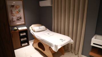 A small, private room with a wooden bench, a white table with a towel, and a shelf with branded towels.