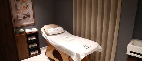 A small, private room with a wooden bench, a white table with a towel, and a shelf with branded towels.