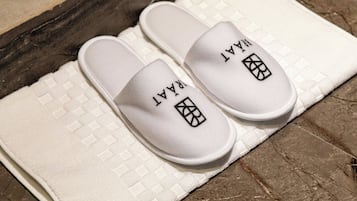 A pair of white slippers with a logo on the front, placed on a textured white towel on a stone floor.
