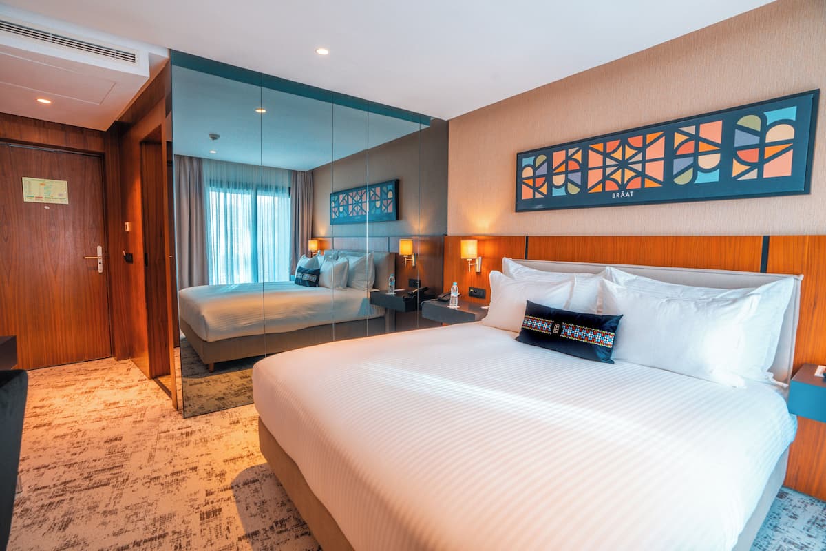 Habitación de hotel con dos camas, un espejo grande, una obra de arte en la pared y un cabecero de madera.