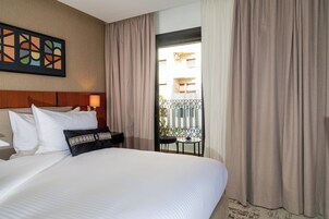 Habitación de hotel con una cama grande, cabecero, un cuadro en la pared y vistas a un balcón con cortinas.