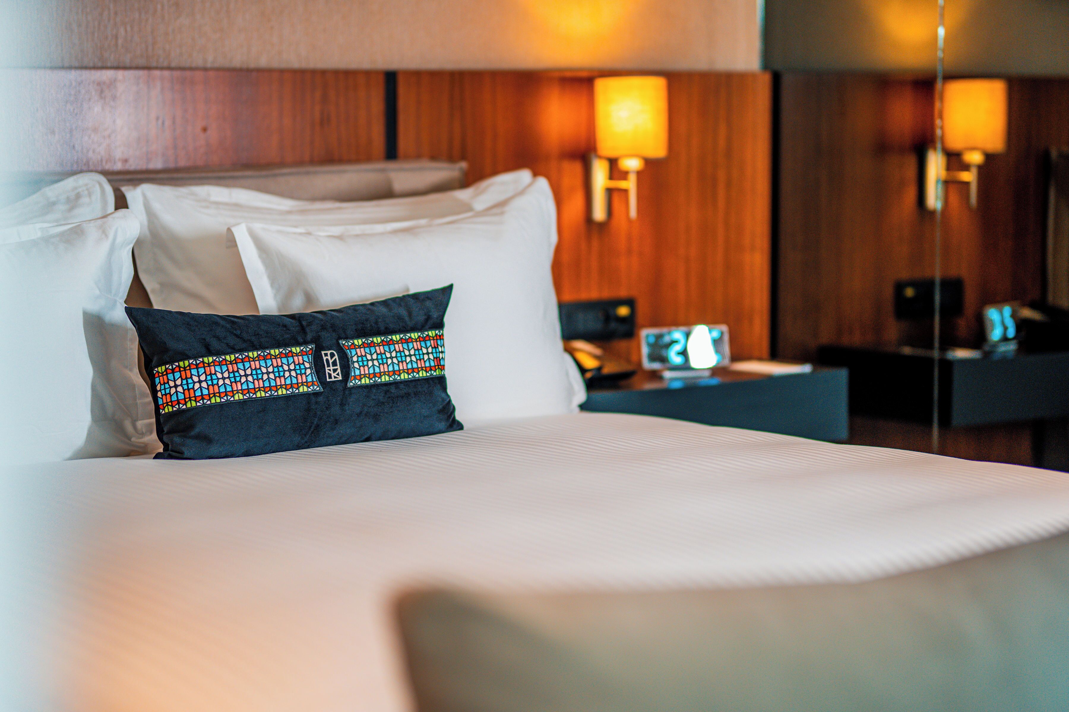 Una habitación de hotel con una cama bien hecha, una mesita de noche con lámpara y un cabecero de madera.
