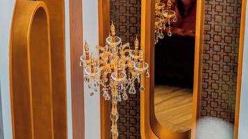 A luxurious room with a large mirror, a chandelier, and a red leather bench.