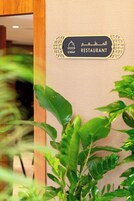 Un letrero de restaurante con texto en árabe e inglés, rodeado de plantas de interior.
