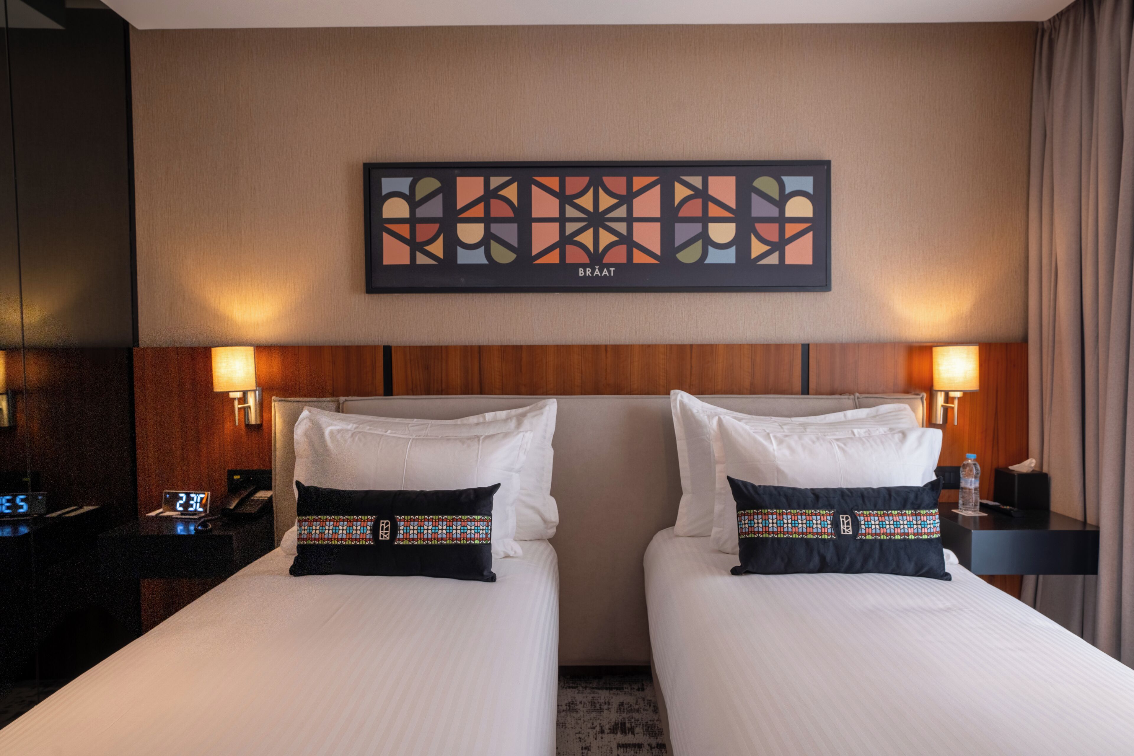 Habitación de hotel con dos camas, una obra de arte en la pared, lámparas de noche y un reloj.