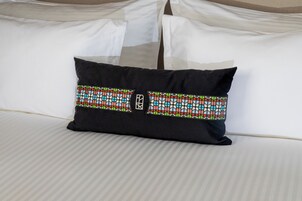 A bed with white linens and a black pillow with a colorful geometric pattern.