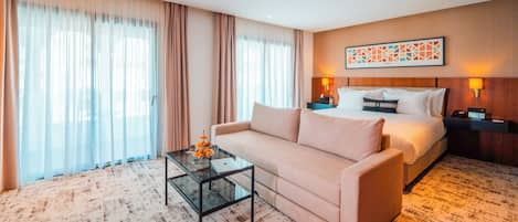 A hotel room with a bed, a sofa, a glass coffee table, and a large window with curtains.