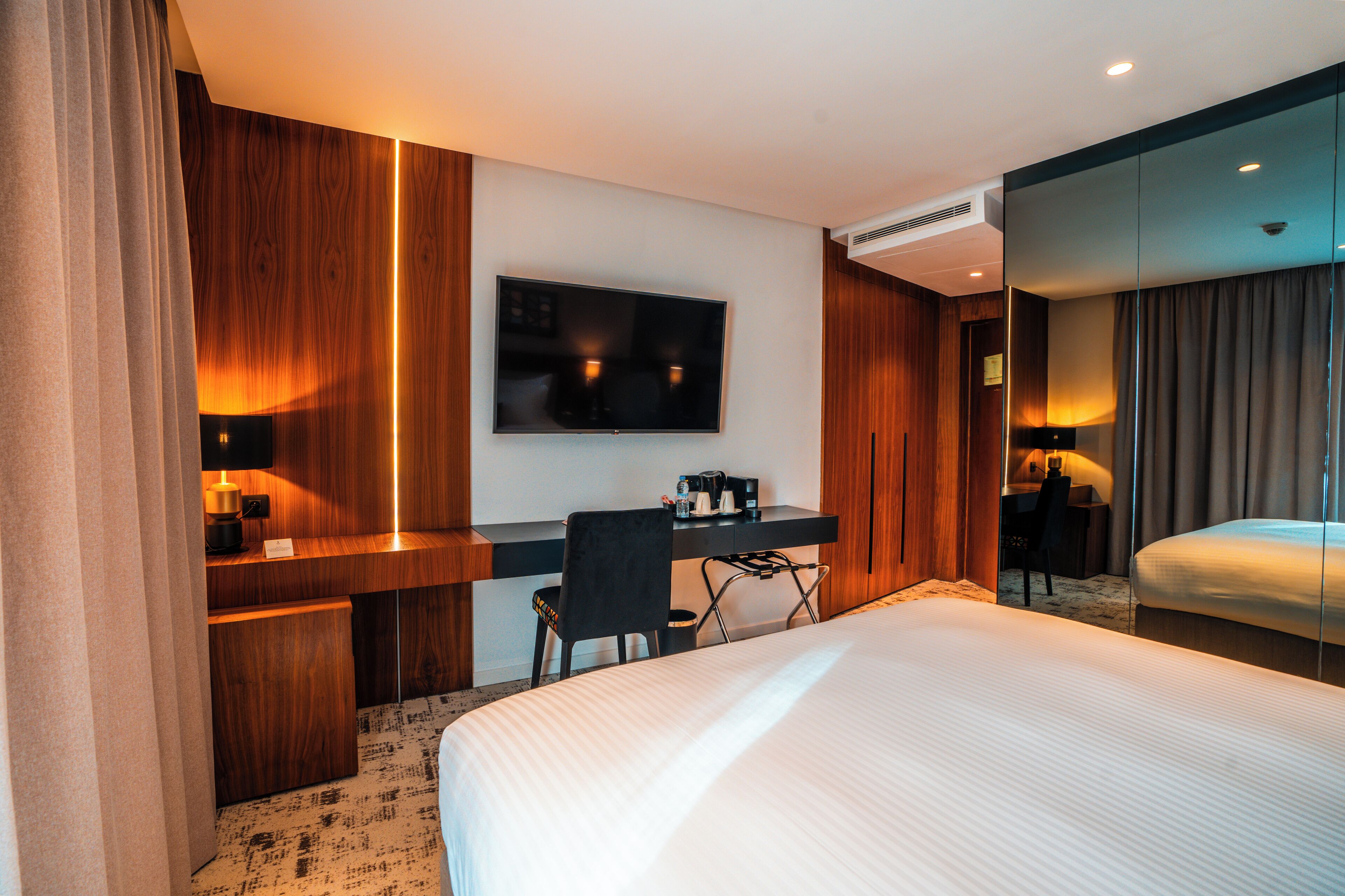 A hotel room with a bed, a desk, a chair, a television, and a mirror.