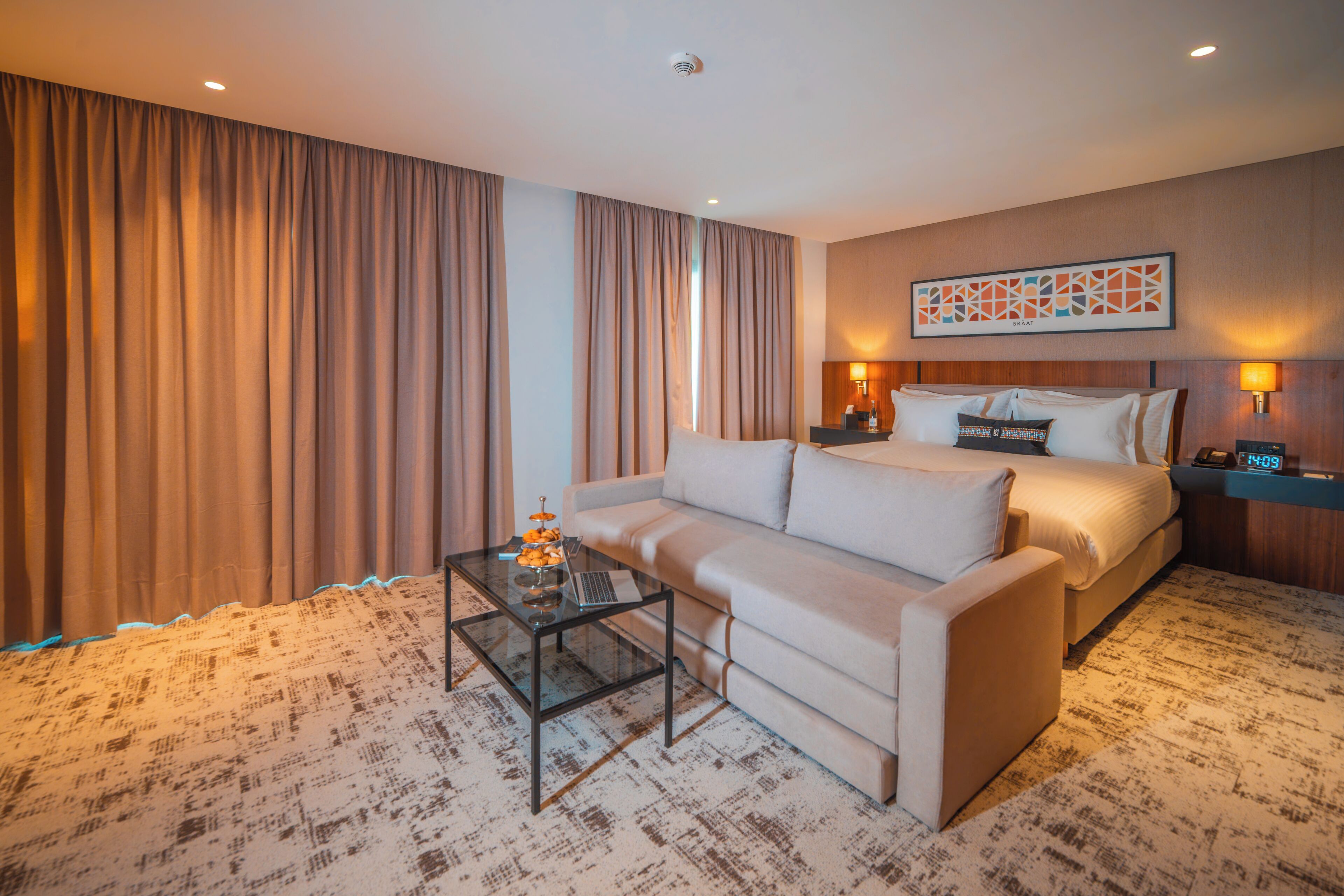 A hotel room with a bed, a sofa, a coffee table, and a painting on the wall.