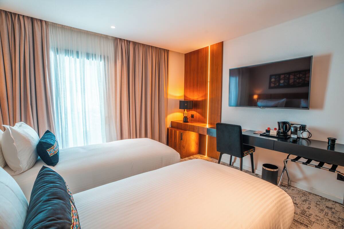 Habitación de hotel con dos camas, un escritorio, una silla, un televisor y una lámpara.