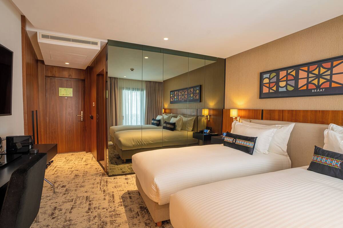 Habitación de hotel con dos camas, un escritorio, un espejo y una obra de arte colgada en la pared.