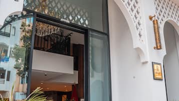 Entrada de um edifício moderno com porta de vidro, design de treliça branca e uma palmeira em vaso.