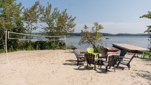 A beach volleyball net with chairs and a dock by a lake.