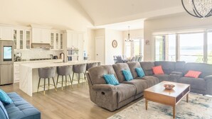 A spacious living area with a large sofa, a coffee table, and a kitchen with a central island and bar stools.