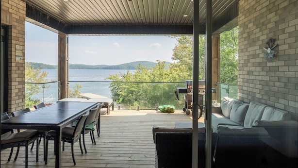 A covered outdoor deck with a table and chairs, a sofa, and a view of the water and mountains.