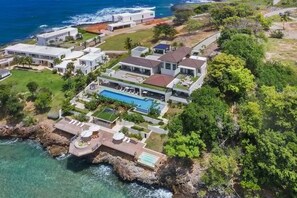 A coastal property with multiple houses, a swimming pool, and a rocky shoreline. - Gorgeous Beach House Perched Right Over the Ocean (Samaná)