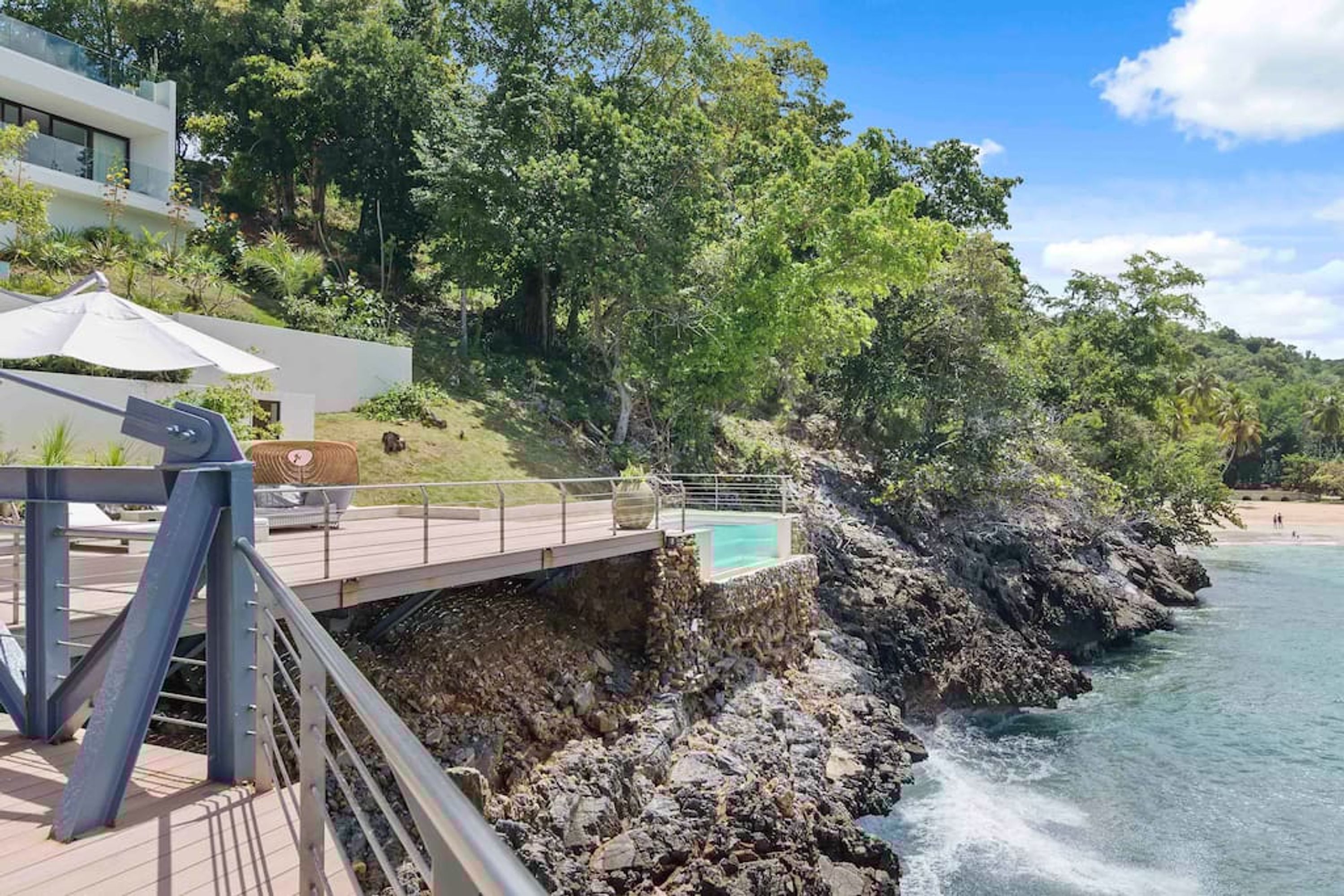 A coastal property with a wooden deck, a swimming pool, and a rocky shoreline.