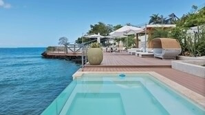 A poolside area with a wooden deck, lounge chairs, and umbrellas. - Gorgeous Beach House Perched Right Over the Ocean (Samaná)