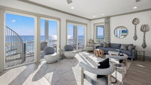 A spacious living room with large windows, a balcony, and a view of the sea.