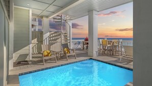 A pool area with a view of the ocean at sunset, wooden deck chairs, and a spiral staircase.
