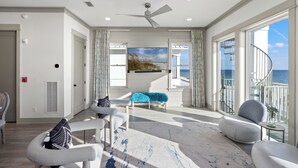 A spacious living room with a large window, a ceiling fan, and a view of the ocean.