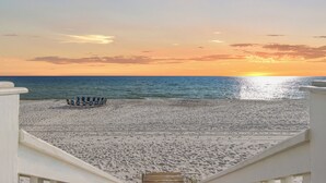 A beach with a row of blue chairs and a wooden deck leading to the water.