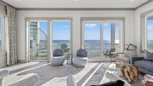 A spacious room with a large sliding glass door leading to a balcony with a view of the ocean. There are two armchairs, a sofa, and a small table with a lamp.