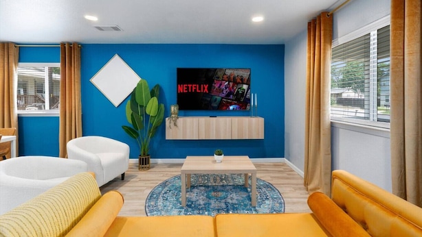 Ett modernt vardagsrum med en blå accentvägg, en Netflix-skylt, ett träskåp, ett runt soffbord och en stor växt.