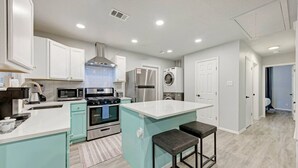 A modern kitchen with white cabinets, a central island, a stainless steel refrigerator, and a built-in oven. - Private Pool & Games - Pet-Friendly Fun Stay Mins to Downtown & Airport (Austin)