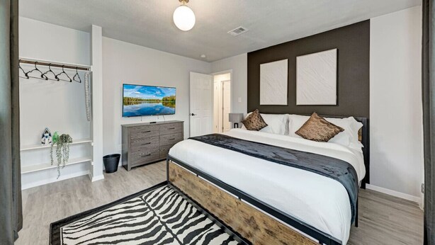 A modern bedroom with a large bed, a TV, a dresser, and a wooden floor. - Private Pool & Games - Pet-Friendly Fun Stay Mins to Downtown & Airport (Austin)