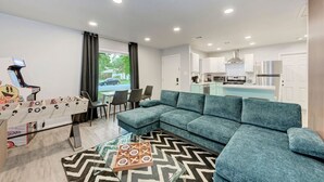 A modern living room with a sectional sofa, a foosball table, and a dining area with chairs and a table. - Private Pool & Games - Pet-Friendly Fun Stay Mins to Downtown & Airport (Austin)