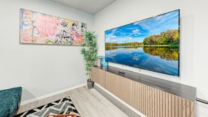 A modern living room with a large flat-screen TV mounted on the wall, a colorful abstract painting above it, and a potted plant beside the TV. - Private Pool & Games - Pet-Friendly Fun Stay Mins to Downtown & Airport (Austin)