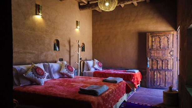 A traditional room with two beds, a wooden door, and a hanging light fixture. - Land of dreams (Nekob)