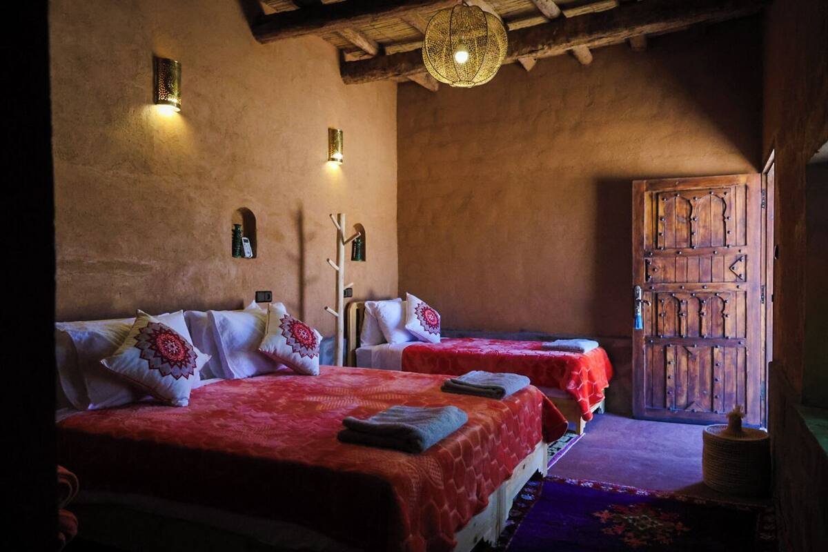 A traditional room with two beds, a wooden door, and a hanging light fixture.