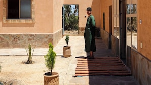 A building with a flat roof, large windows, and a courtyard with potted plants and a striped rug. - Land of dreams (Nekob)