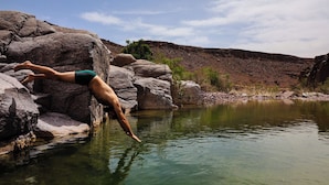 A person diving into a clear pool surrounded by large rocks and a hilly landscape. - Land of dreams (Nekob)