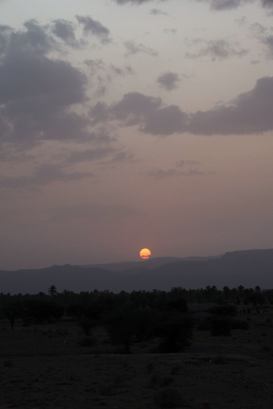 Un tramonto su un paesaggio piatto con colline in lontananza e vegetazione rada.