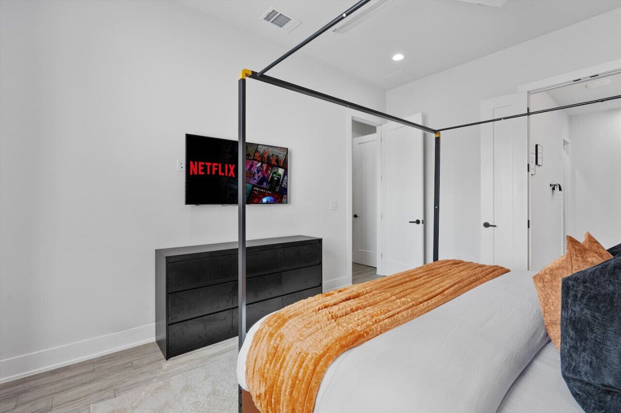 A modern bedroom with a four-poster bed, a black TV on the wall, and a wooden floor.