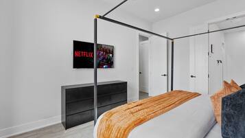 A modern bedroom with a four-poster bed, a black TV on the wall, and a wooden floor.