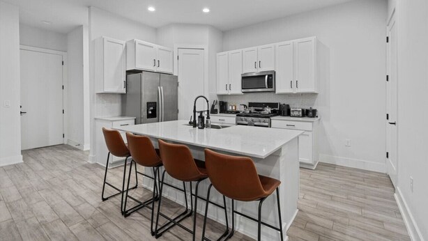 A modern kitchen with white cabinetry, a central island with bar stools, stainless steel appliances, and a light wood floor. - Modern Austin Getaway & Near Downtown, Lake Travis & Event Venues! (Austin)