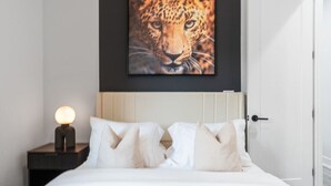 A hotel room with a bed, white bedding, a nightstand with a lamp, and a framed picture of a leopard on the wall. - Modern Austin Getaway & Near Downtown, Lake Travis & Event Venues! (Austin)