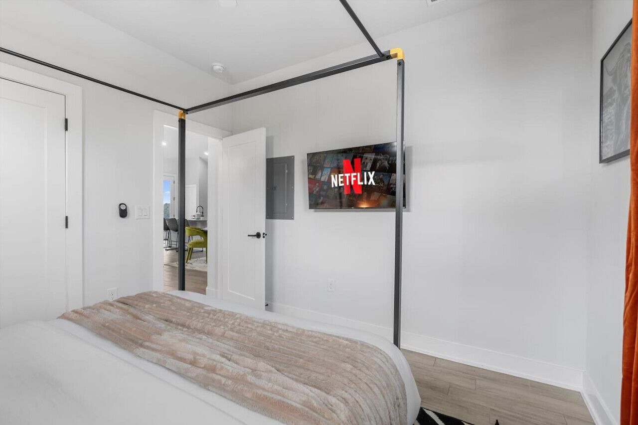 Una camera da letto con un letto a baldacchino, un'uscita che dà su un balcone e una TV a parete con il logo Netflix.